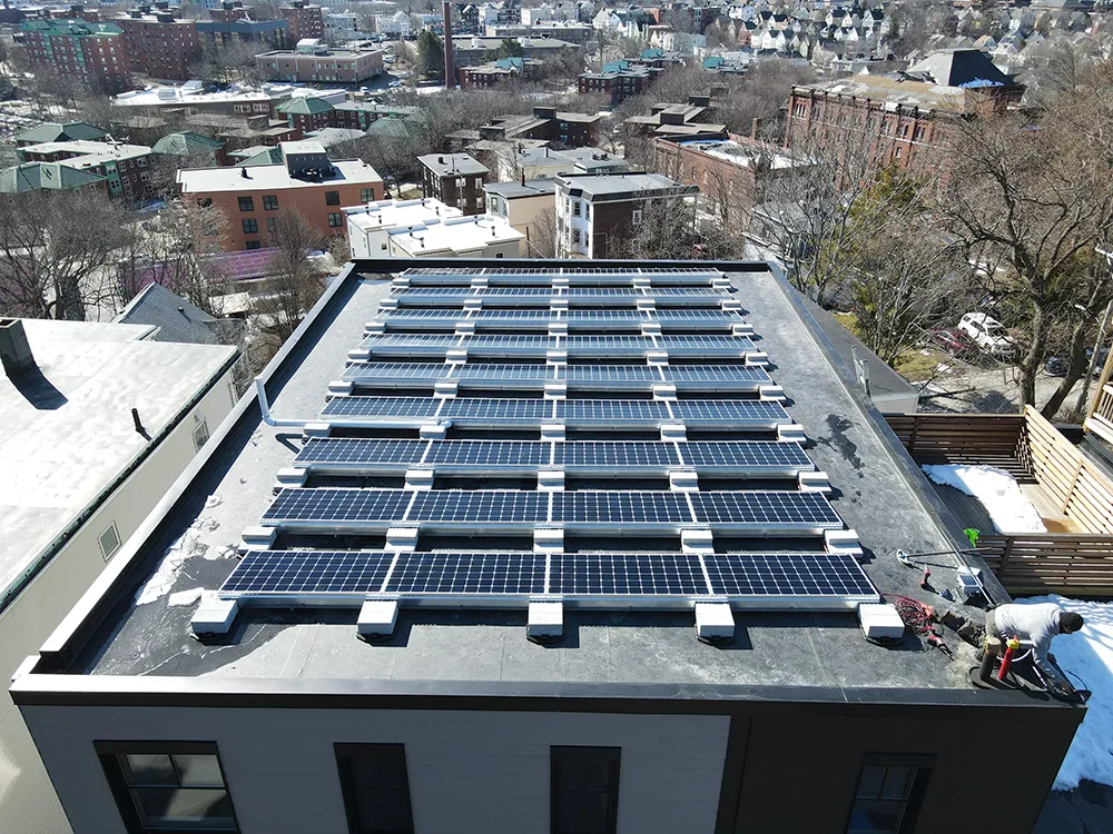 Man working to install solar panels on the roof of 52 Fisher Ave in Boston, MA