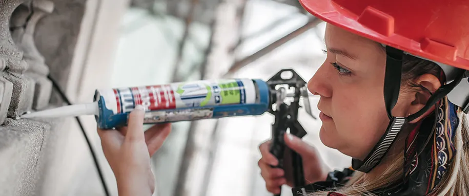 Female construction mason on the scaffolding, working with silicone gun